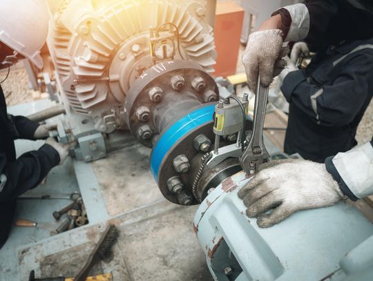 Two maintenance workers performing upkeep on the same piece of machinery while wearing white work gloves.