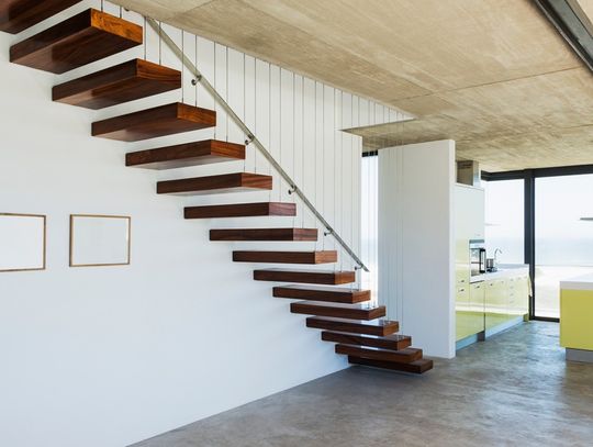 A floating staircase featuring dark red wood and a metal handrail in a modern, spacious, well-lit home