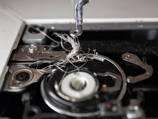 An extreme close-up shot of the interior of a sewing machine that holds the bobbin. It is tangled with white thread.