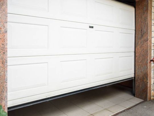 An individual is pointing a small garage door opener at a white garage door. The door is raised off the ground.