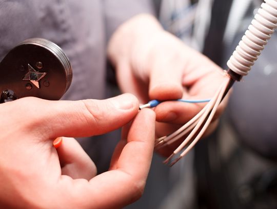 A close-up of an electrician's hands adjusting the end of an insulated wire while holding a manual crimper.