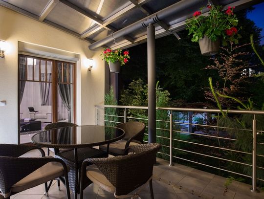 Two sconces illuminate a covered patio at night. A round table with four chairs sits on the tiled patio.