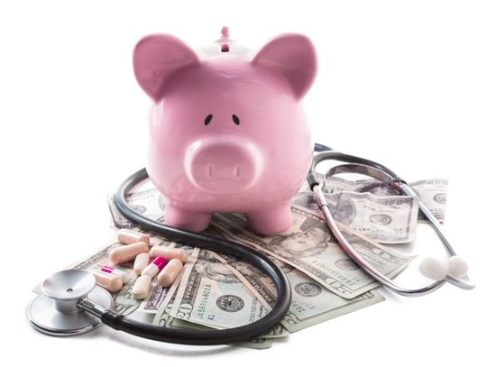 A pink piggy bank is sitting on top of a stack of money, a stethoscope, and a handful of medication.