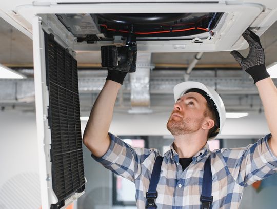 A close-up of an HVAC technician using his tools and repairing an air conditioner unit on the ceiling.