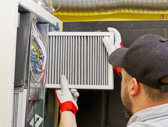 A man wearing a black hat and white and red gloves replacing the white filter in a ventilation system.