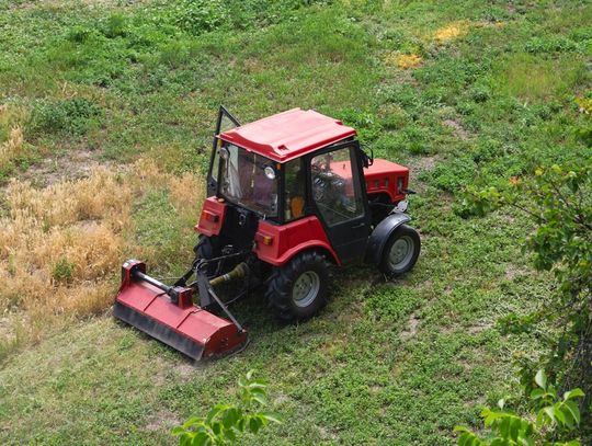 An overhead view of a red tractor with a brush cutter attachment. The tractor is driving through a green field.