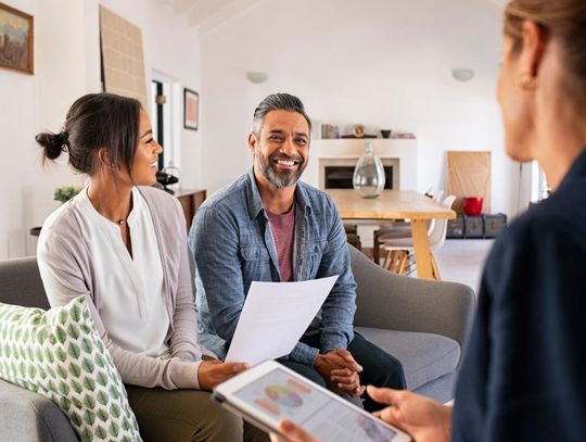 A couple is talking to a financial advisor at home. The husband and wife are smiling and laughing together.