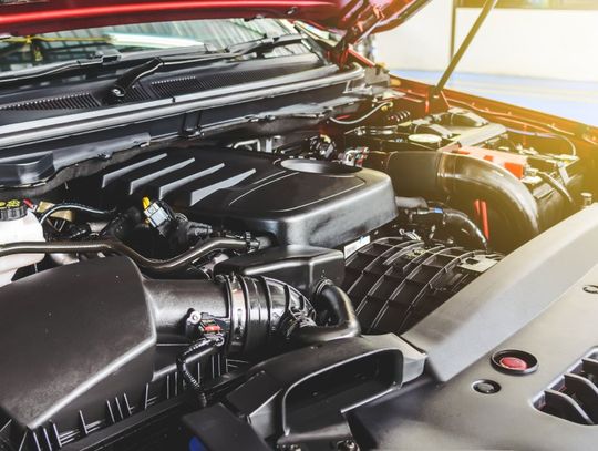 A close-up of the exposed engine bay of a red pickup truck. The displayed components appear clean and new.