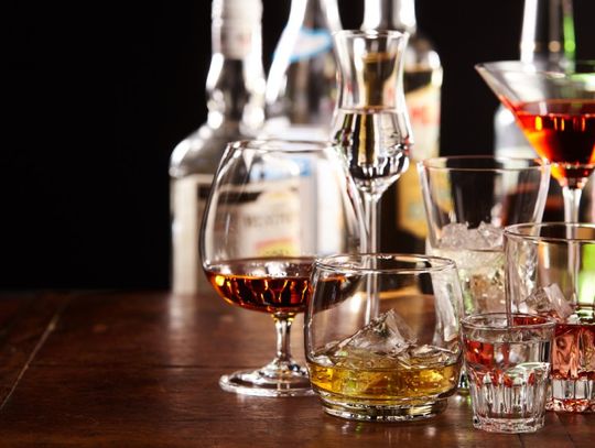 An assortment of cocktails in different glasses, from shot glasses to martini glasses, on a wooden table.