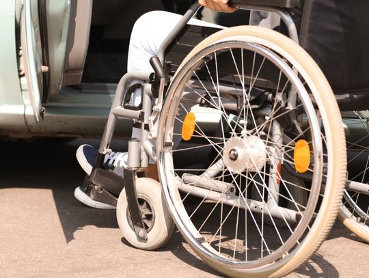 A close-up of the wheels of a wheelchair as the user approaches the open door of a car's driver's side.