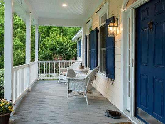 A southern Mississippi home with a large, wrap around front porch. The porch has two white wicker chairs.
