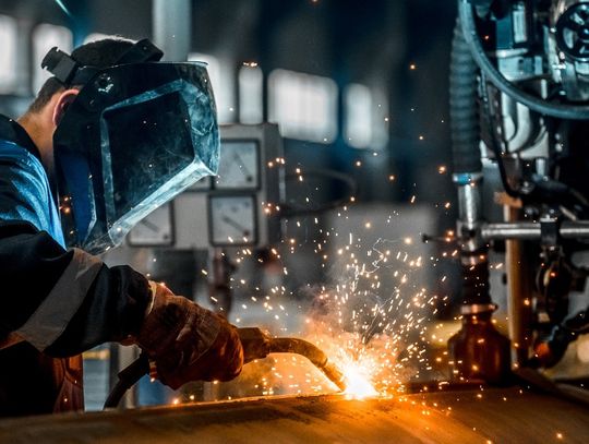 A man in a welder's mask using a welding torch to connect two different sections of a large pipe together.