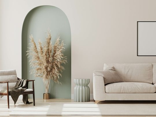 A living room with modern furniture and a decorative green arch with dried flowers, a white sofa, and an armchair.