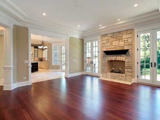 A living room in a residential home. The floor is made of hardwood and there is a stone fireplace against the wall.