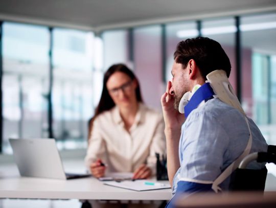 A personal injury lawyer at the back of the table with a laptop, sitting with a client who is wearing a neck brace.