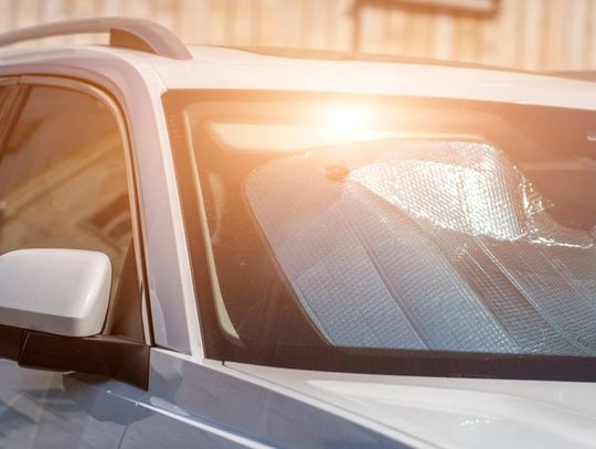 A silver car sits in a parking lot. The sun creates a warm glow and reflects off of the vehicle's sun visor on the windshield.