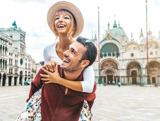 A man gives his female partner a piggyback ride through a European city center. They smile as they take in the sites.
