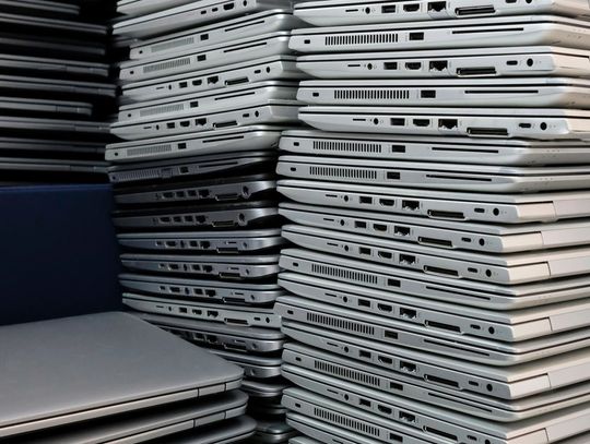A close-up of dozens of silver laptops. They're arranged in four towering stacks and showing cable ports.