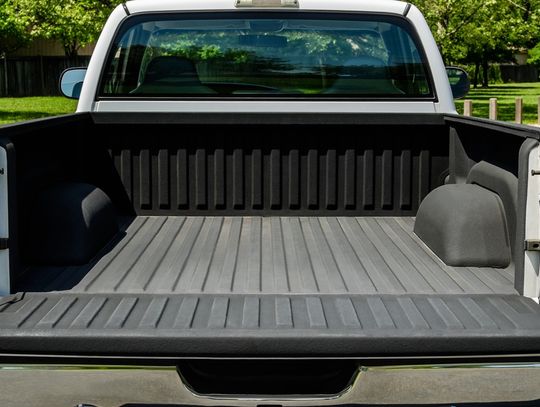 A white pickup truck with its tailgate down. The truck bed is empty and has an upgraded liner installed onto it.