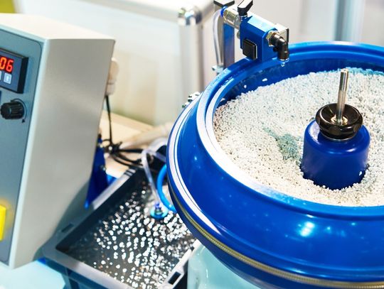 A blue vibratory finishing bowl full of small media in a factory. A small tank of water connects to the finishing bowl.
