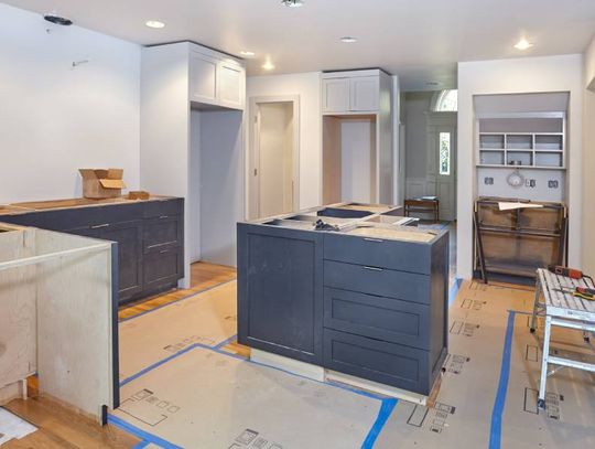 Custom cabinets being installed in a kitchen, some finished and some unfinished. Cardboard is laid out on the floor.