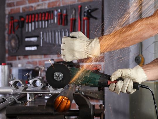 A man wearing white protective gloves operates an industrial metal cutting saw to cut through a metal pipe.