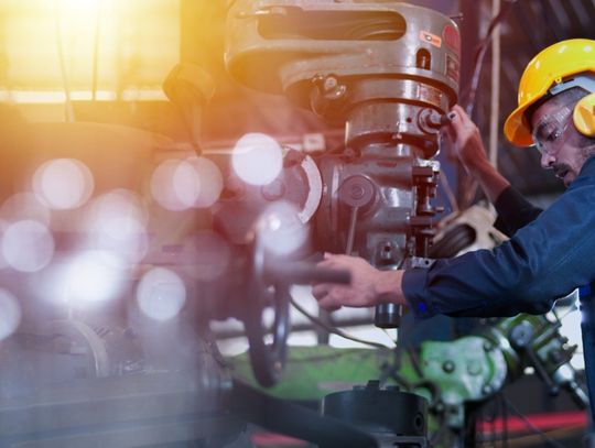 A factory worker wearing a hard hat and ear protection while he is working with a large piece of machinery.