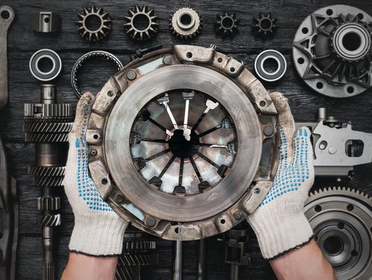 An overhead view of a person with white gloves holding a clutch basket over a black table with other clutch parts.