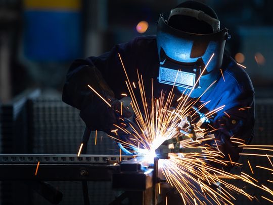 A person who is wearing a protective mask is using an arc welder on a piece of material.