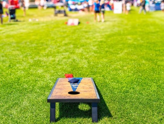 At a large outdoor gathering, there is a cornhole board in a field with two bags sitting on top of it.