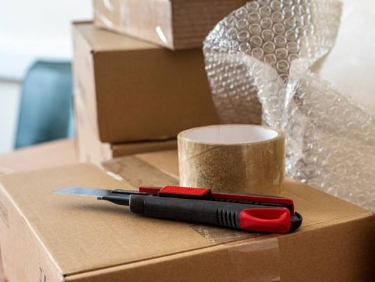 A selection of packaging and shipping supplies, such as a cardboard box, packing tape, bubble wrap, and a box cutter.