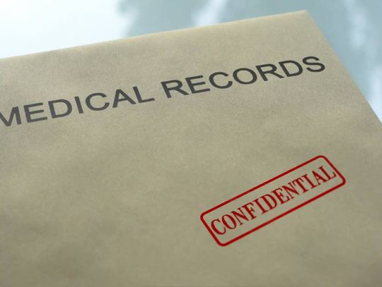 A tan folder labeled Medical Records with a red confidential stamp resting on a reflective glass tabletop.