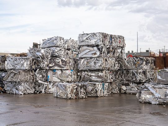 Numerous bales of aluminum and metal scrap are stacked on top of each other outside in a recycling yard.