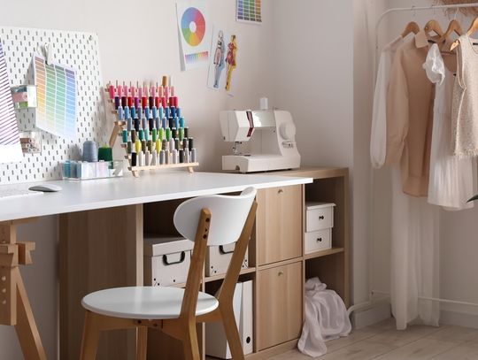 A white table next to a wall with a matching chair, holding multiple colored threads, a sewing machine, and some boxes.