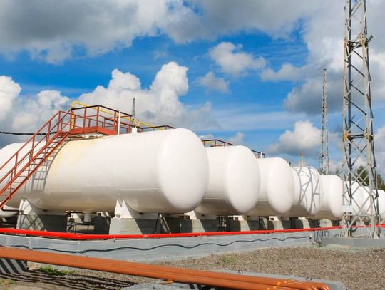 Multiple gasoline storage tanks sit horizontal and are all next to each other on a large concrete slab.