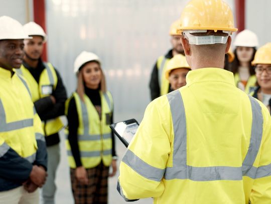 Seven employees on a construction site looking at a site manager who is speaking to the entire group.