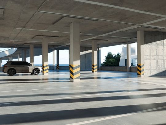 A gray car parked alone between two pillars in a parking garage. Bright sunlight shines into the parking structure.