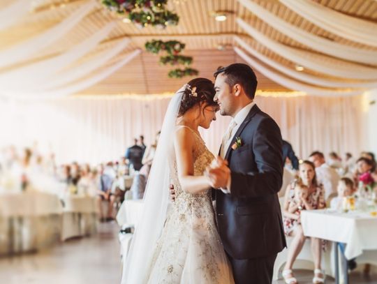 A bride and groom dancing on the dance floor in a large wedding venue. The guests sit at their tables.