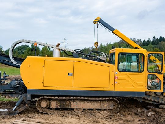 A yellow horizontal directional drilling machine drills on the ground underneath a bright blue sky.