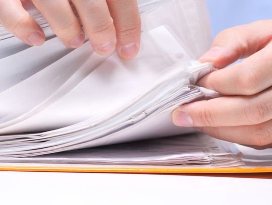 Close-up of a person's fingers flipping through various documents that are in clear plastic sleeves.