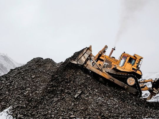 A large yellow bulldozer moves mining debris into a hill in an industrial mining area covered in snow.