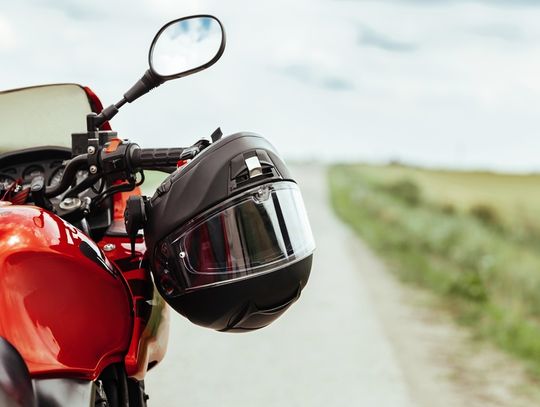 A close-up shows a black motorcycle helmet hanging on the right handlebar of a stationary red motorcycle.