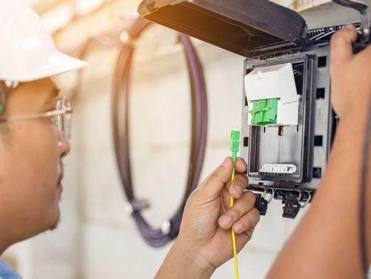 A fiber internet technician connecting a cable to the modem box mounted on the outside of the house.