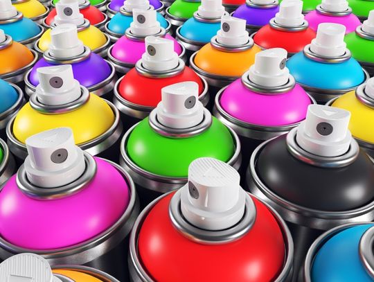 A close-up of the nozzles and top parts of many differently and brightly colored aerosol spray cans in a group.