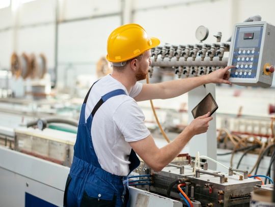 A male factory worker operating machinery using a tablet and a control panel with a digital display.
