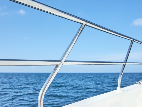 A close-up view shows a shiny stainless steel boat railing on a white boat that is out on a large body of water.