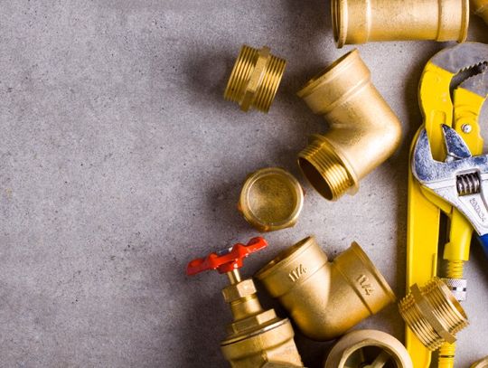 A yellow and a blue wrench, a pair of working gloves, and brass fittings placed on a rough, textured floor.