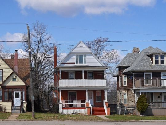 A row of three slightly older looking houses on a street block. There are trees in between each house.