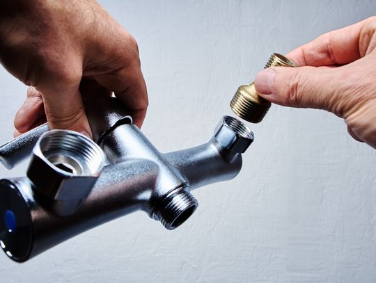 A person attaching a threaded brass component to a silver plumbing fixture in front of a white background.