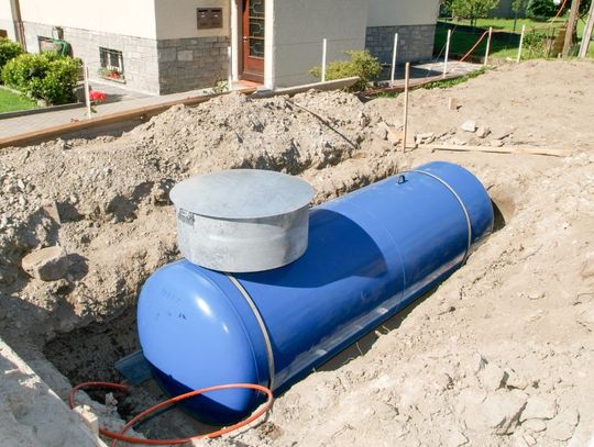 A tank that is underground and surrounded by a pile of dirt. The tank is blue, and there's a cord near it.